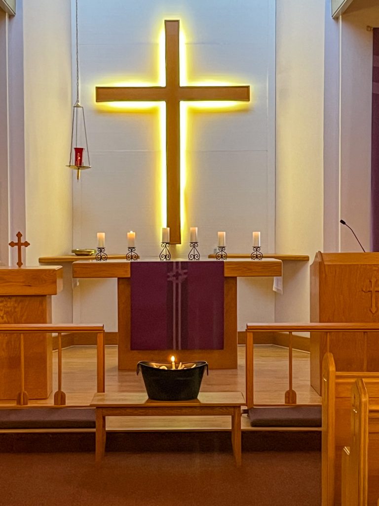 altar with small lit candles and an illuminated cross.